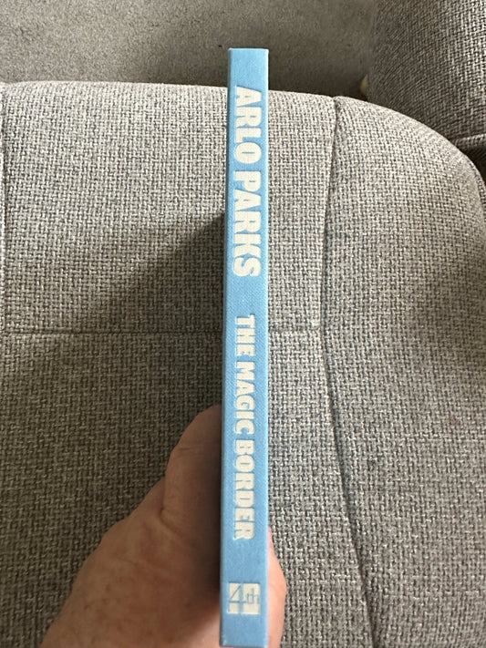 Side view of The Magic Border signed poetry book by Arlo Parks in blue binding on a textured surface