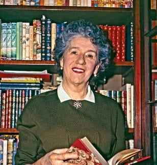 Portrait of Enid Blyton holding a book in front of shelves filled with books Enid Blyton biography