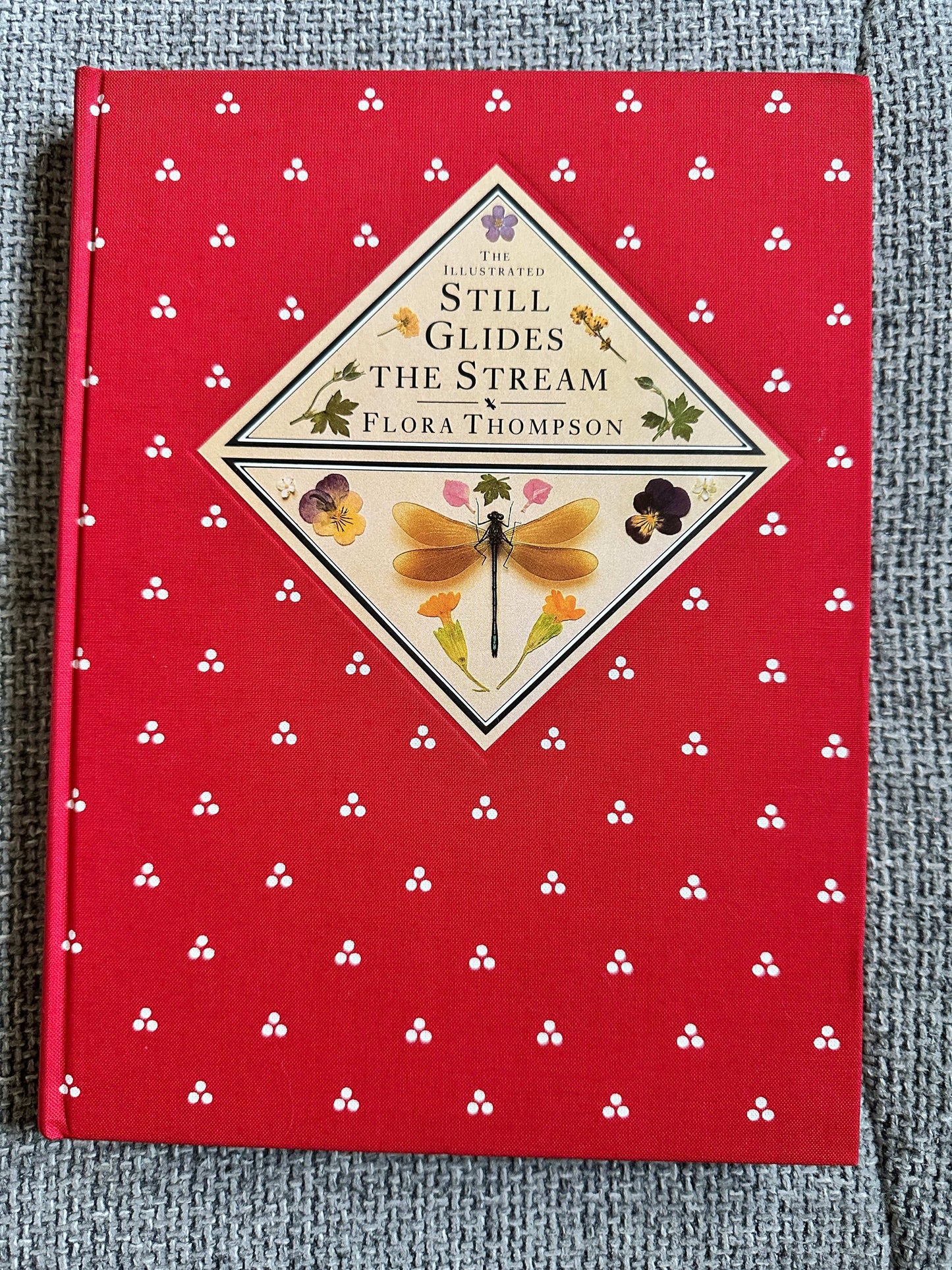 The illustrated edition of Still Glides The Stream Flora Thompson with a red floral cover design