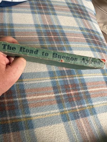 The Road to Buenos Ayres rare book with a worn spine held by a hand against a plaid backdrop