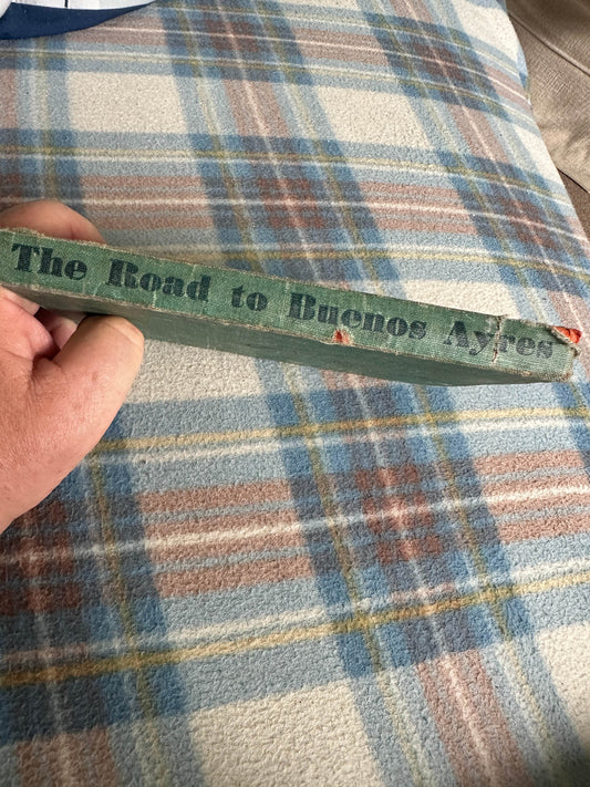 The Road to Buenos Ayres rare book with a worn spine held by a hand against a plaid backdrop